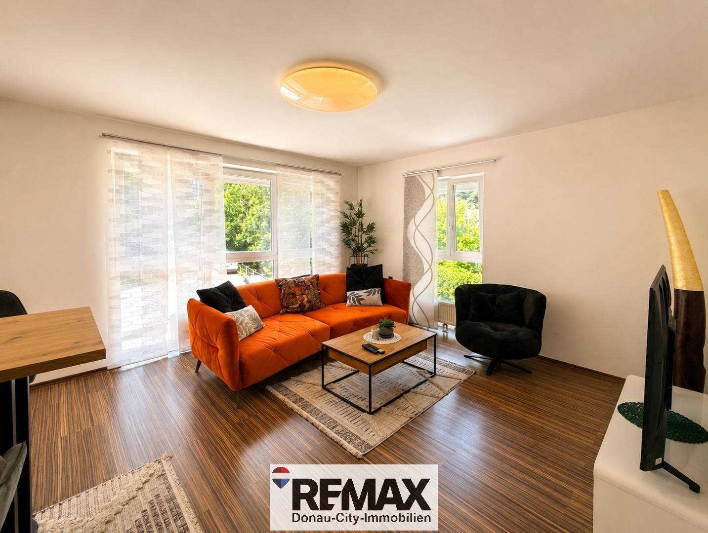 Helles Wohnzimmer mit großzügigen Fenstern, modernem Sofa und Holzboden.