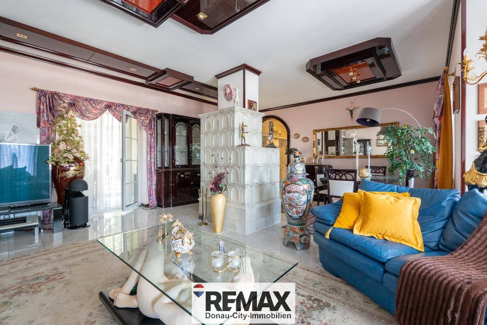 Gemütliches Wohnzimmer mit blauem Sofa, gläsernem Couchtisch und einem traditionellen Kachelofen.
