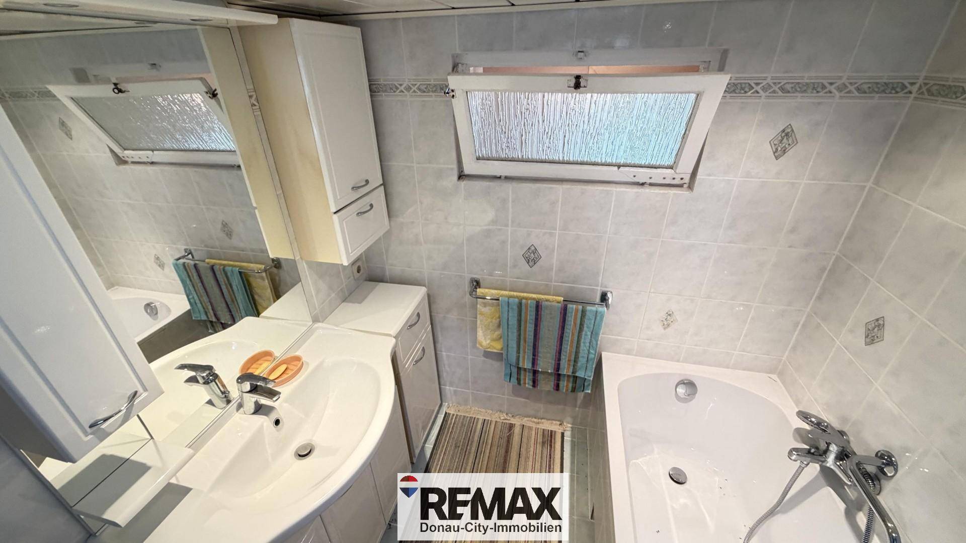 Badezimmer mit Badewanne, Waschbecken und Dachfenster, gefliest in hellen Tönen.