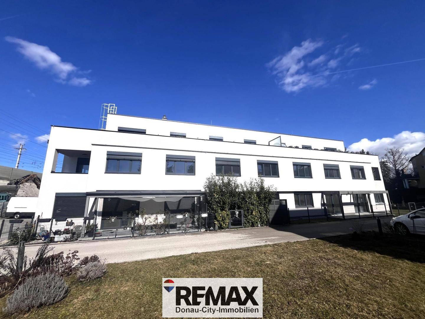 Moderne Wohnanlage mit klarer Architektur und großen Fensterfronten unter blauem Himmel.