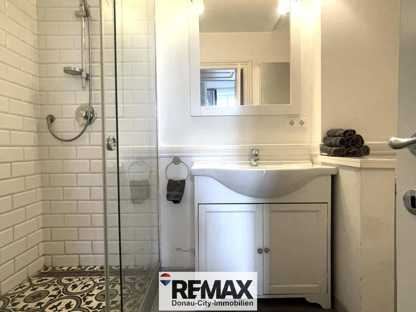 Modernes Badezimmer mit begehbarer Dusche, weißem Waschbecken und dekorativen Fliesen.