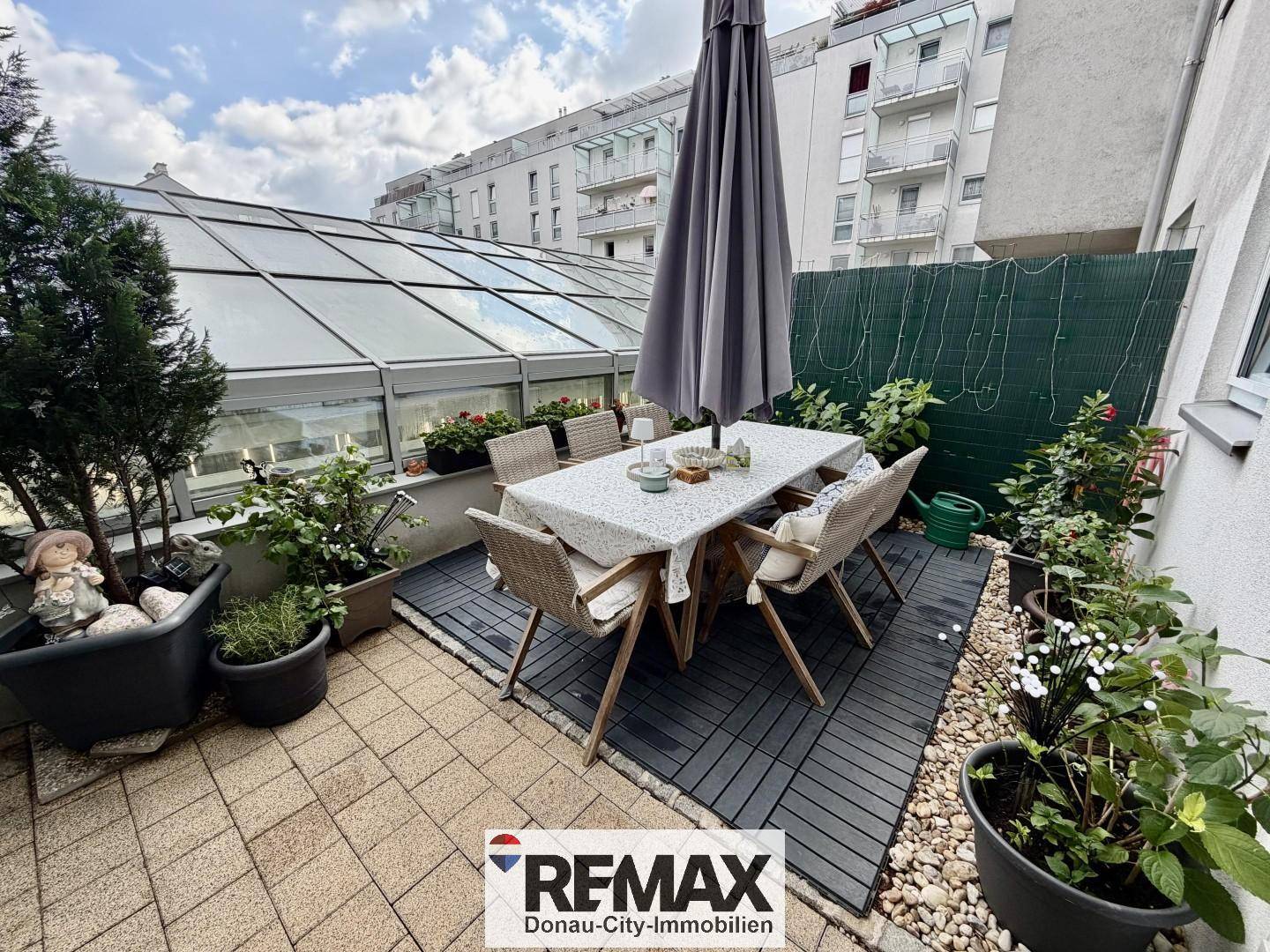 Gemütliche Terrasse mit Esstisch, Sonnenschirm und vielen Pflanzen, ideal für Mahlzeiten im Freien.