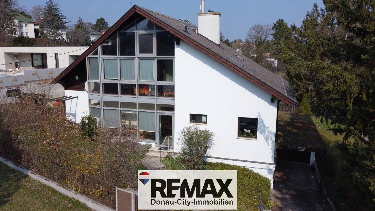 Zeitgenössisches Einfamilienhaus mit markanter Glasfassade und Satteldach, umgeben von Grünflächen.