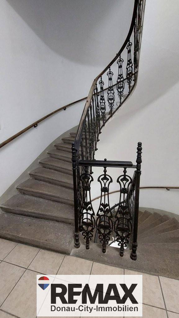 Elegantes Treppenhaus mit geschwungenem schmiedeeisernem Geländer und Steinstufen.