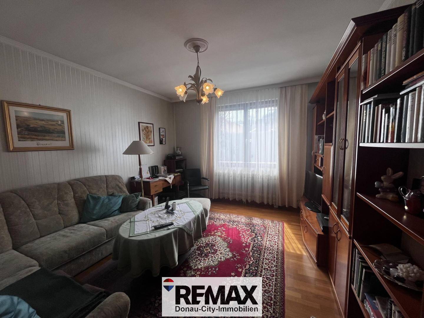Gemütliches Wohnzimmer mit Sofa, großem Bücherregal und Fenster mit Vorhängen.
