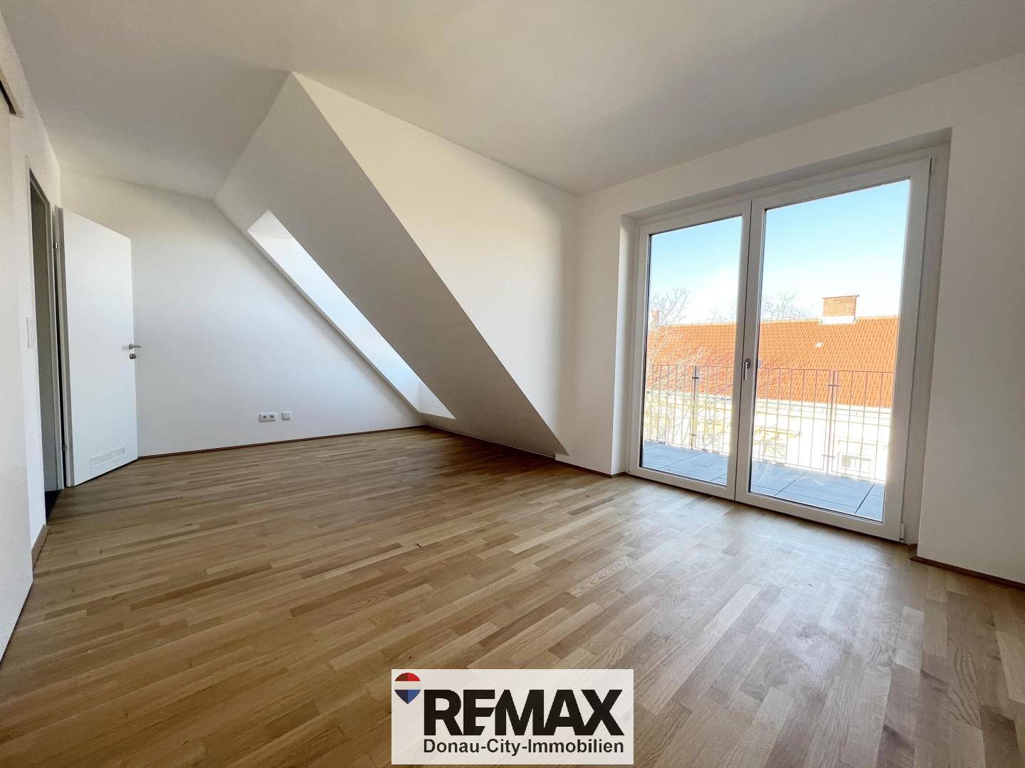 Geräumiges, unmöbliertes Schlafzimmer mit Holzboden, Dachschräge und Balkonzugang.