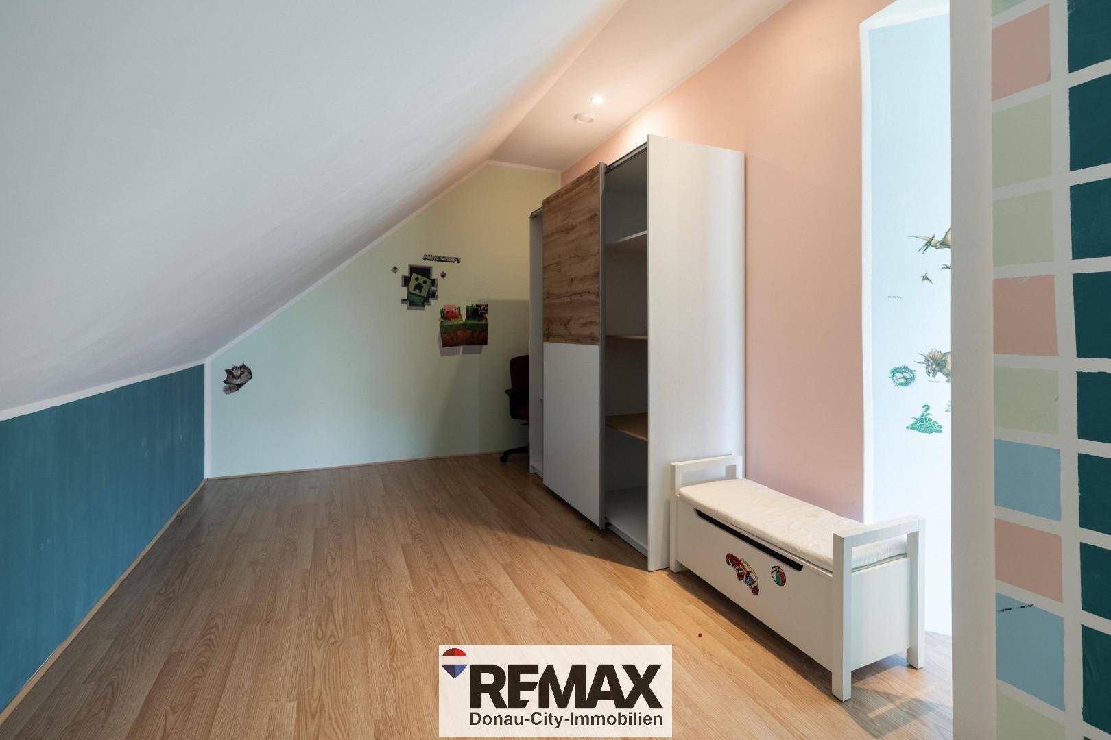 Dachzimmer mit schräger Decke, farbigen Wänden und praktischem Kleiderschrank.