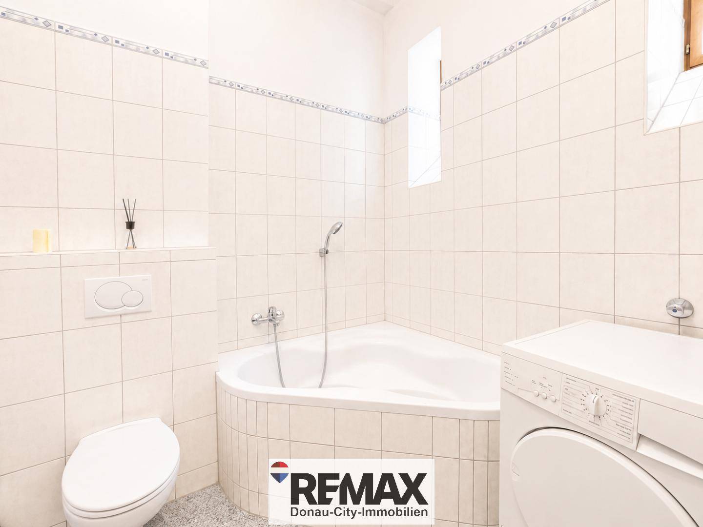 Gefliestes Badezimmer mit Eckbadewanne, Duschfunktion, Toilette und Waschmaschine.