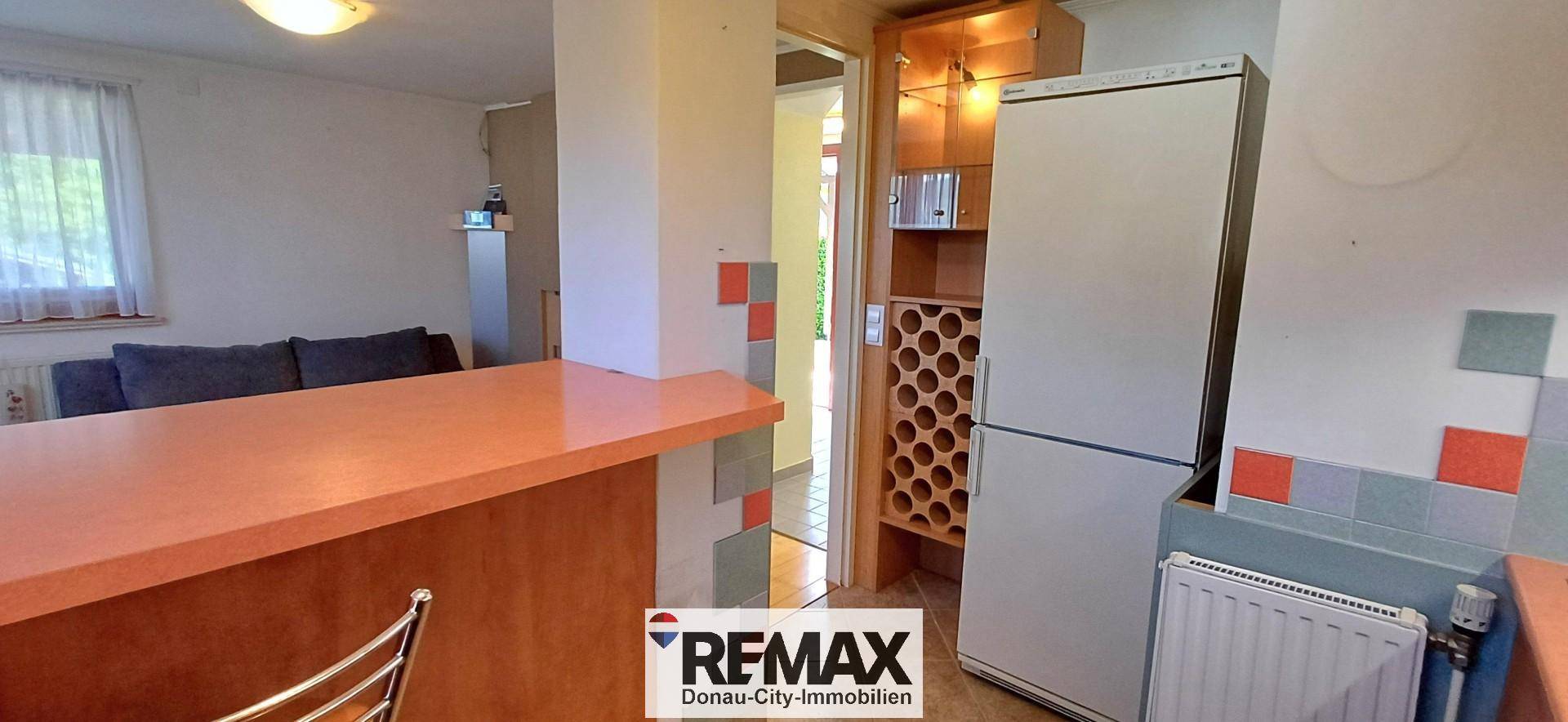 Küchenbereich mit Kühlschrank, Weinregal und einer Theke, die zum Wohnbereich übergeht.