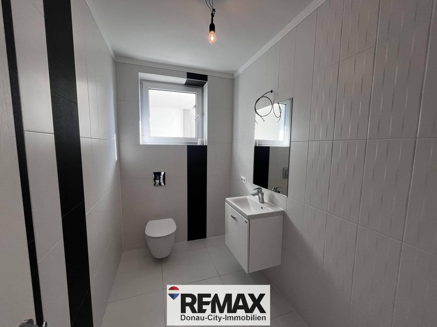 Modernes Gäste-WC mit Wand-WC, Waschbecken und Fenster, in Schwarz-Weiß-Design.