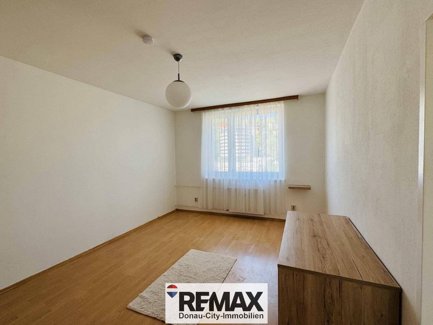 Leeres Schlafzimmer mit hellem Parkettboden und einem Fenster, das Tageslicht hereinlässt.
