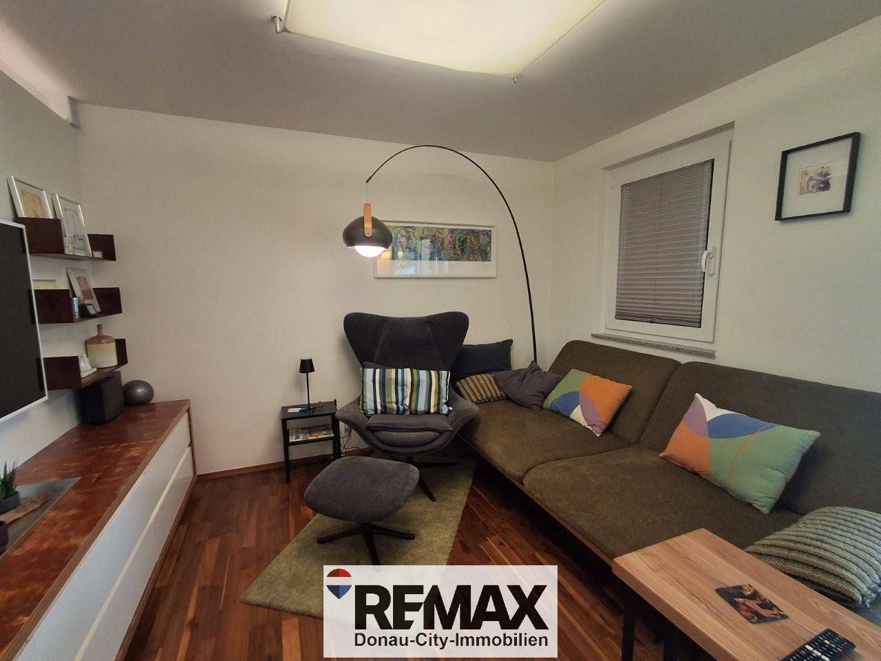 Gemütliches Wohnzimmer mit Sofa, Sessel und einem Fenster mit Jalousien.