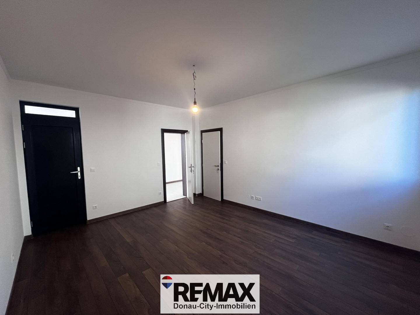 Leeres Zimmer mit dunklem Holzboden und mehreren Türen, bereit zur individuellen Gestaltung.