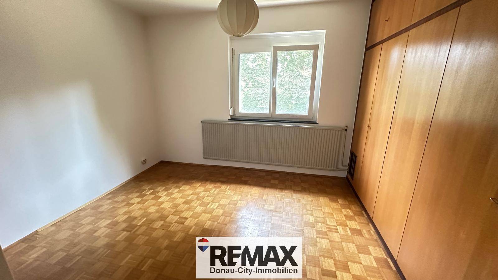 Schlafzimmer mit Parkettboden, Fenster und großem Einbauschrank.