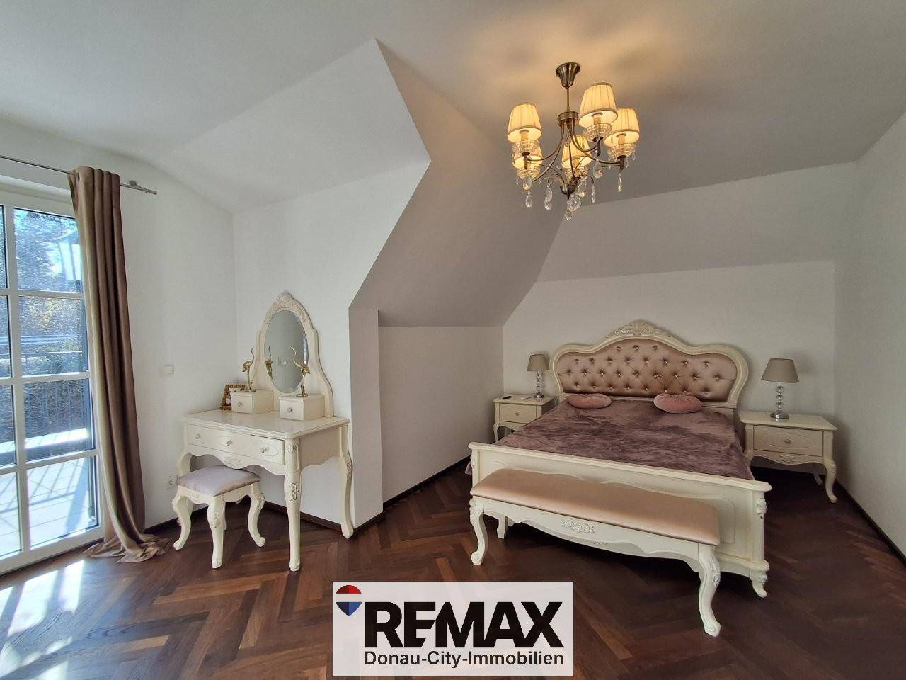 Elegantes Schlafzimmer mit Fischgrätparkett, Schminktisch und Zugang zum Balkon.