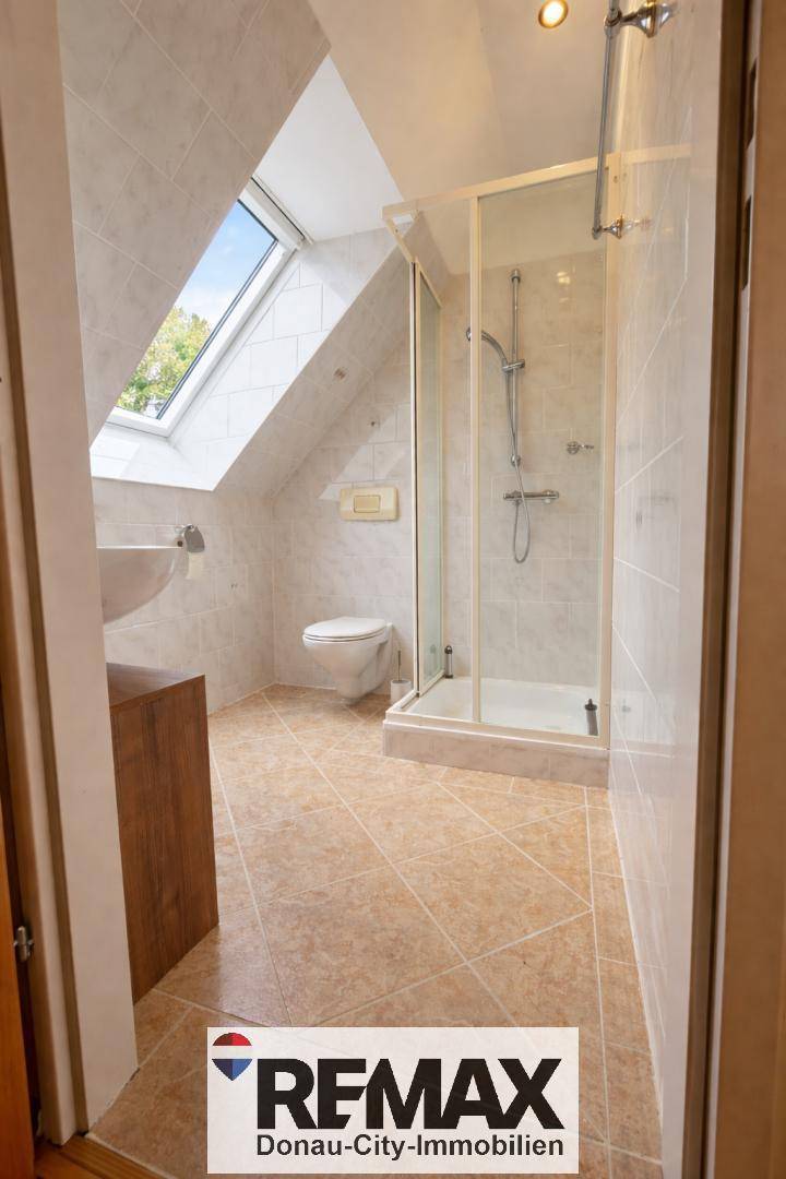 Helles Badezimmer mit Duschkabine, WC, Waschbecken und Dachfenster in der Schräge.