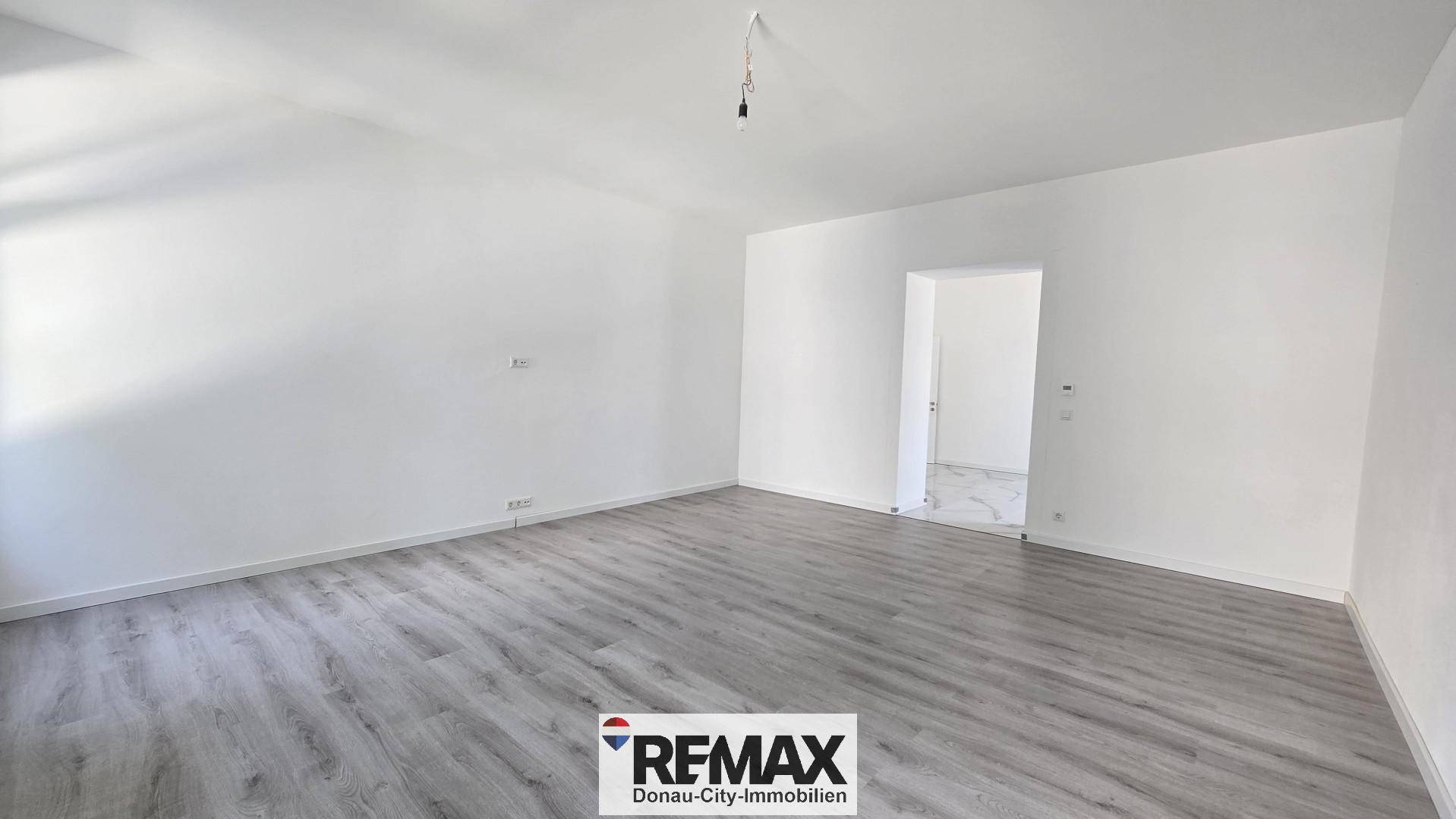 Geräumiger, leerer Raum mit modernem Laminatboden und weißen Wänden, bietet viel Platz.