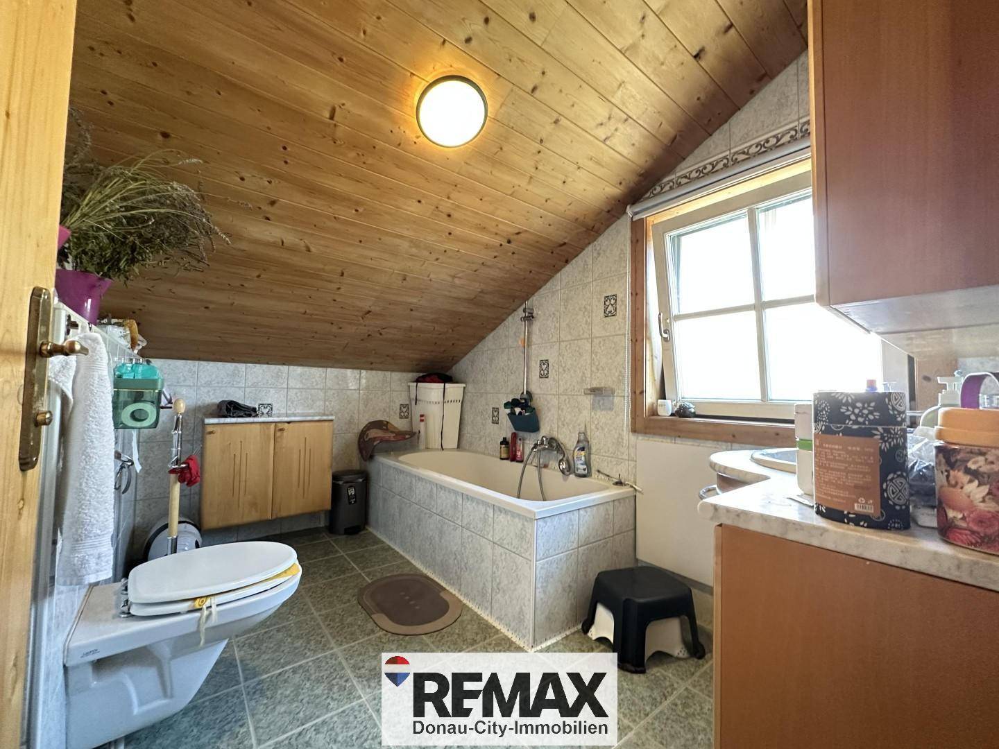 Badezimmer im Dachgeschoss mit Badewanne, WC, Fliesen und Holzdachschräge.