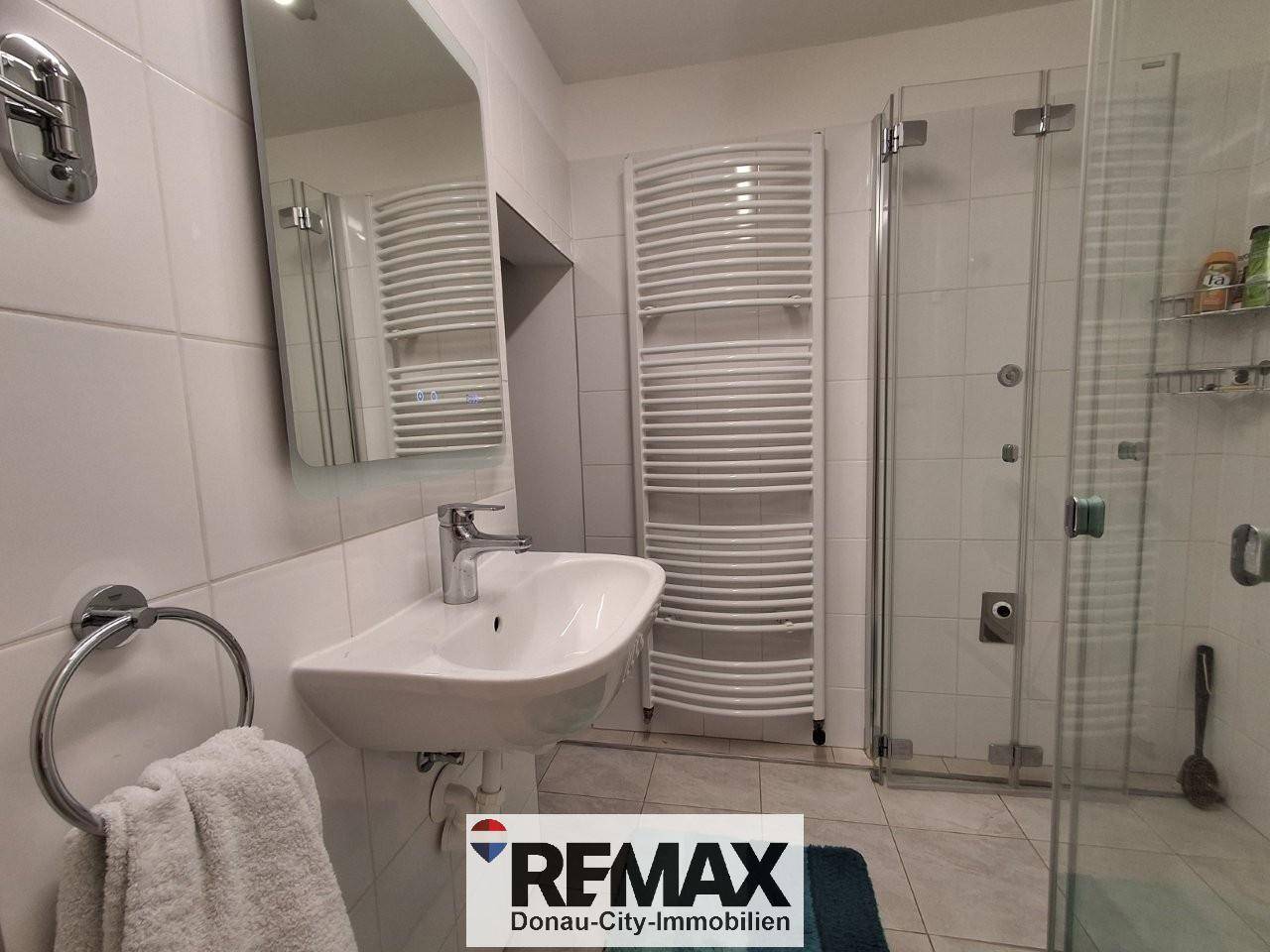 Modernes Badezimmer mit Dusche, Waschbecken, Spiegel und beheiztem Handtuchhalter.