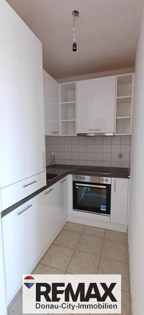 Kleine, funktionale Küche mit weißen Schränken, integriertem Backofen und Fliesenboden.