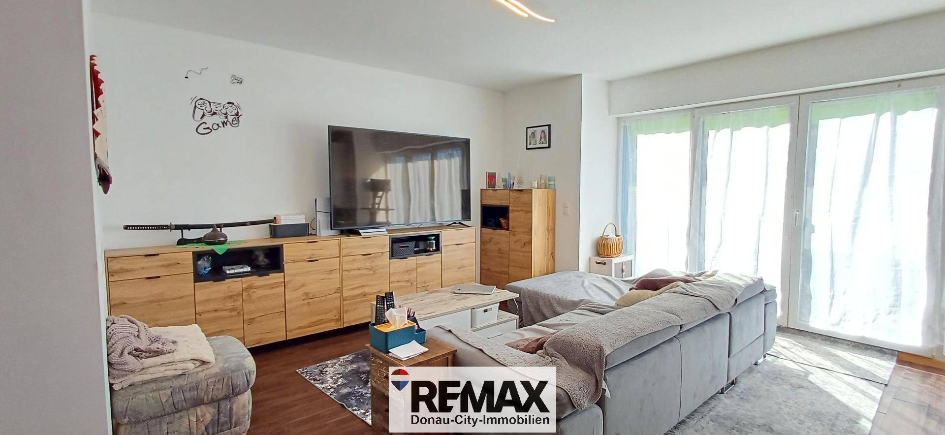 Geräumiges Wohnzimmer mit großem Sofa, Fernseher und Zugang zu einem Balkon oder einer Terrasse.