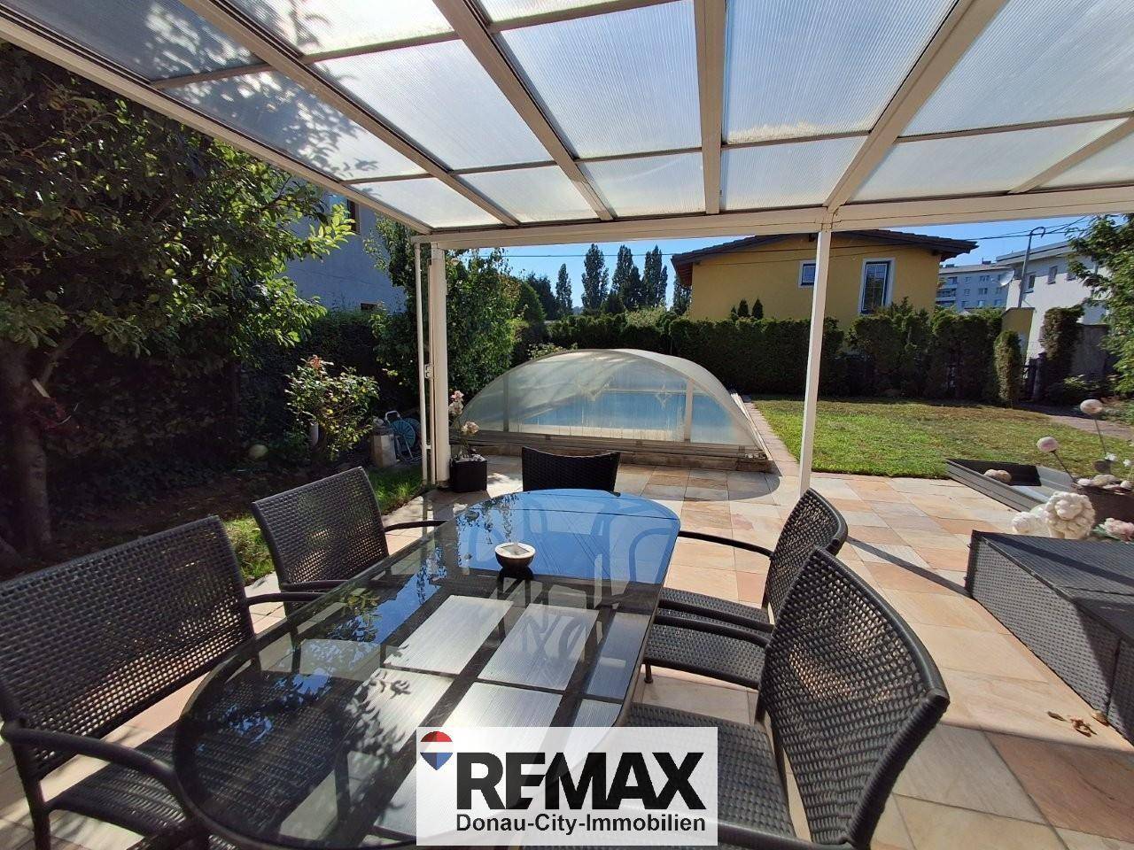 Überdachte Terrasse mit Esstisch und Blick auf den Garten mit einem überdachten Swimmingpool.