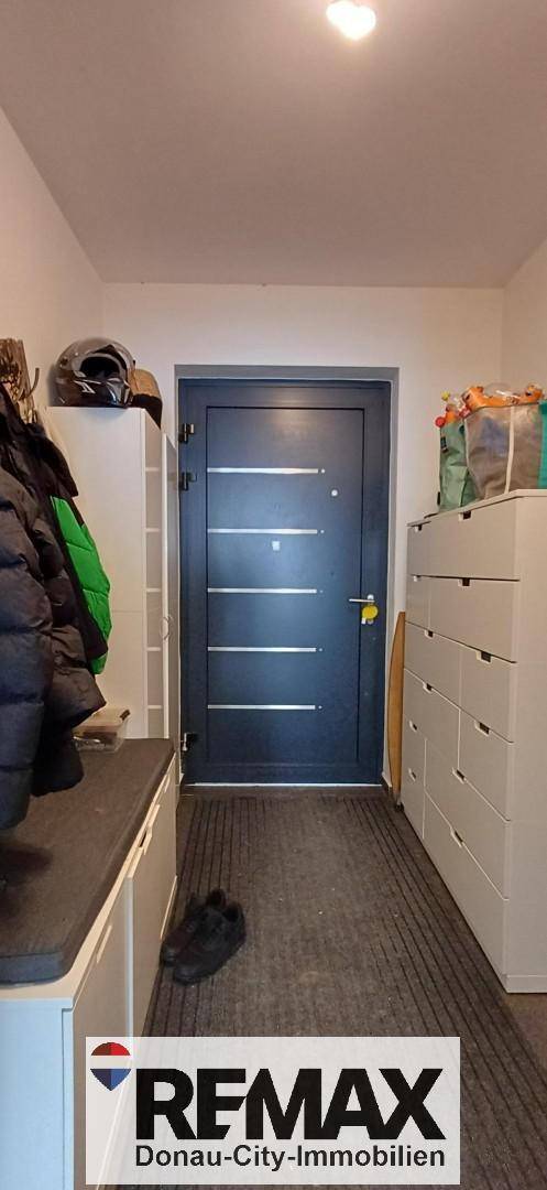 Eingangsbereich mit dunkler Eingangstür, Garderobe und Stauraum.