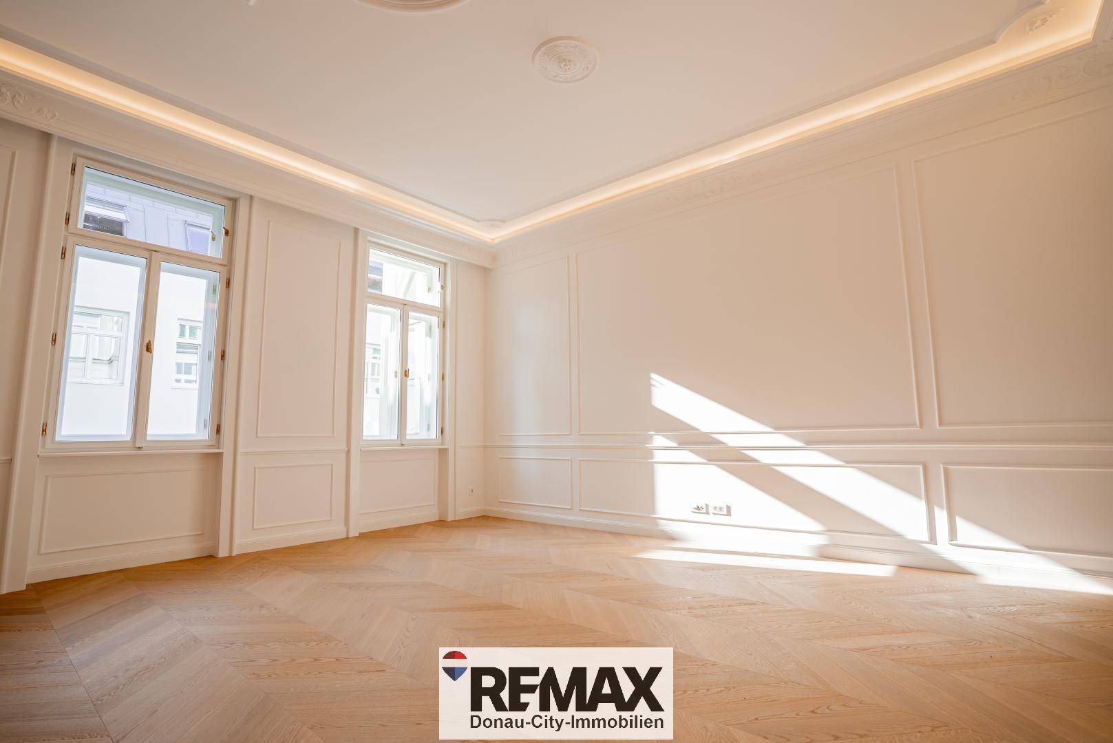 Lichtdurchfluteter Raum mit Fischgrätparkett, hohen Decken und eleganten Wandverkleidungen.
