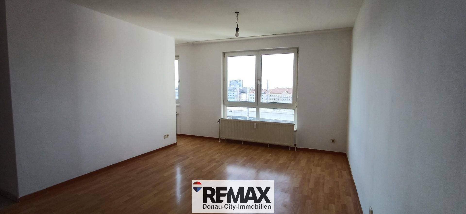 Heller Wohnraum mit Parkettboden, weißen Wänden und großem Fenster.