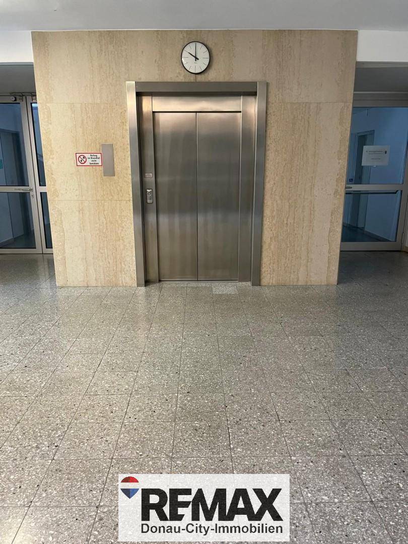 Moderner Aufzug in einer Lobby mit Fliesenboden und einer Uhr über der Tür.