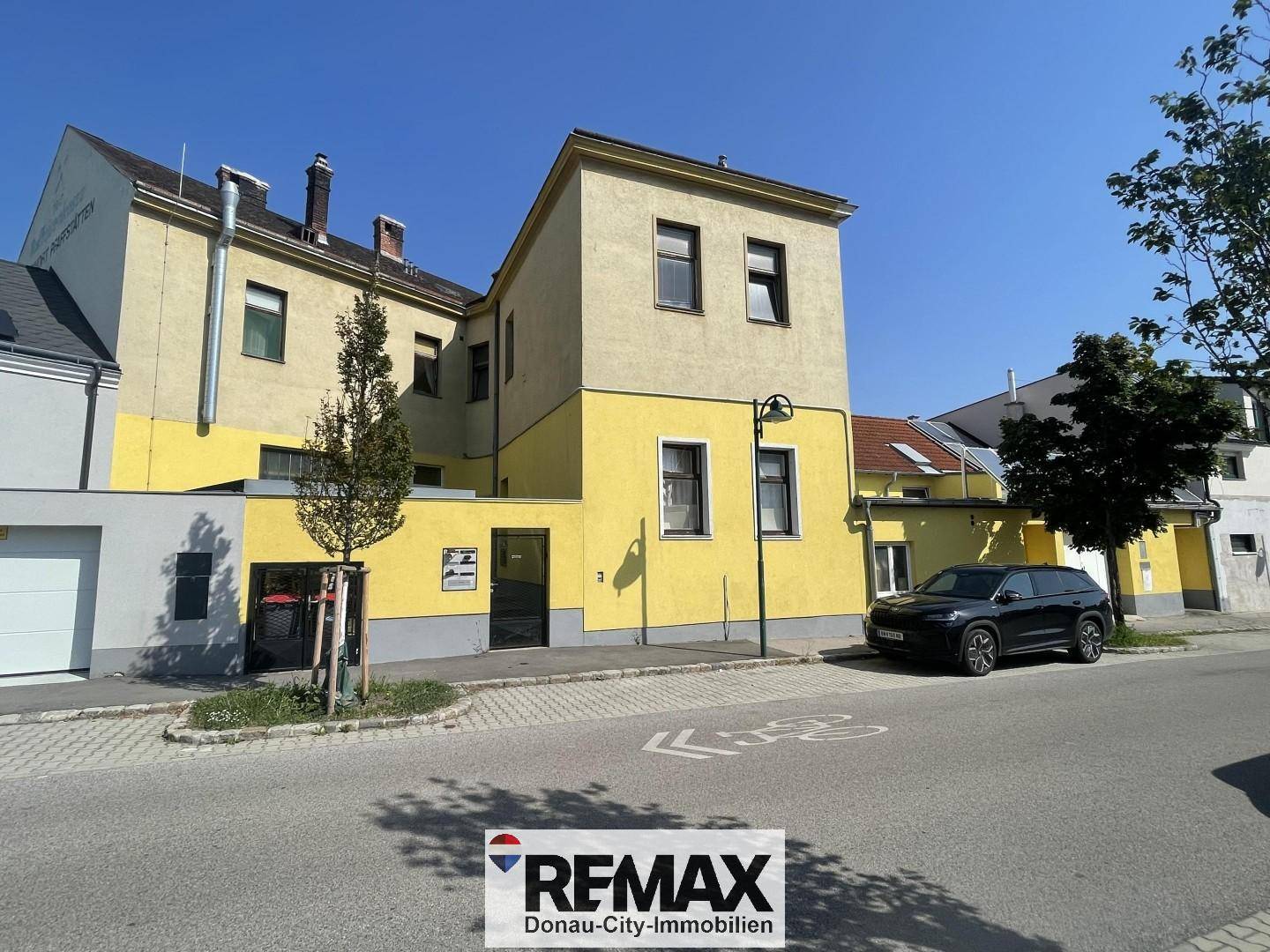 Seitenansicht des Gebäudes mit gelber Fassade, Fenstern und einem geparkten Auto auf der Straße.