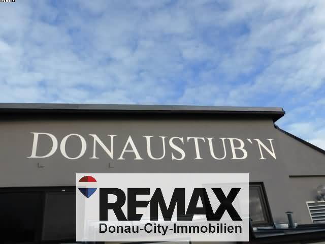 Nahaufnahme des Schriftzugs 'DONAUSTUB'N' an der Fassade des Gebäudes unter blauem Himmel.