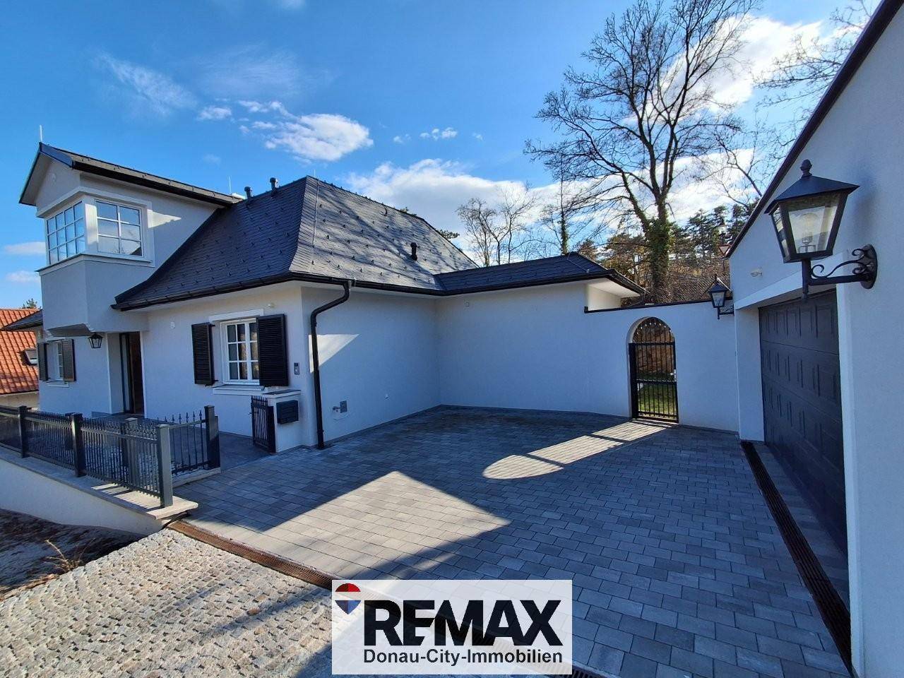 Seitenansicht des Hauses mit gepflastertem Hof, Garagenzufahrt und schmiedeeisernem Tor.