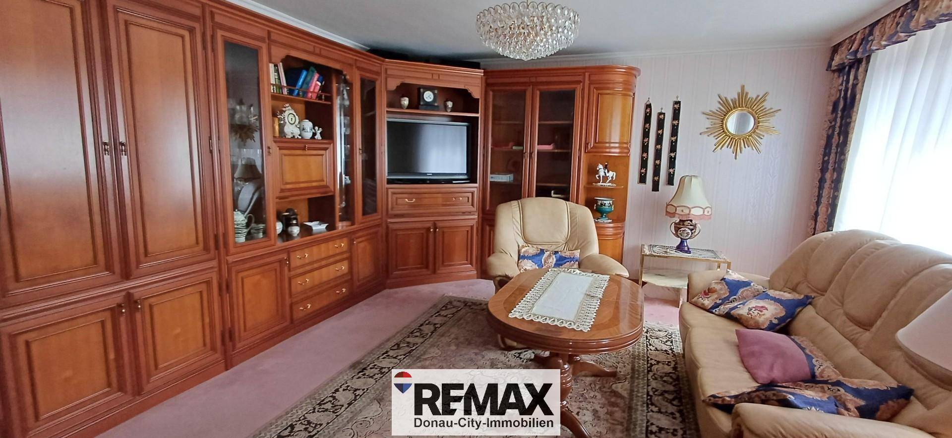 Gemütliches Wohnzimmer mit traditionellen Holzmöbeln, beigem Sofa und Kronleuchter.