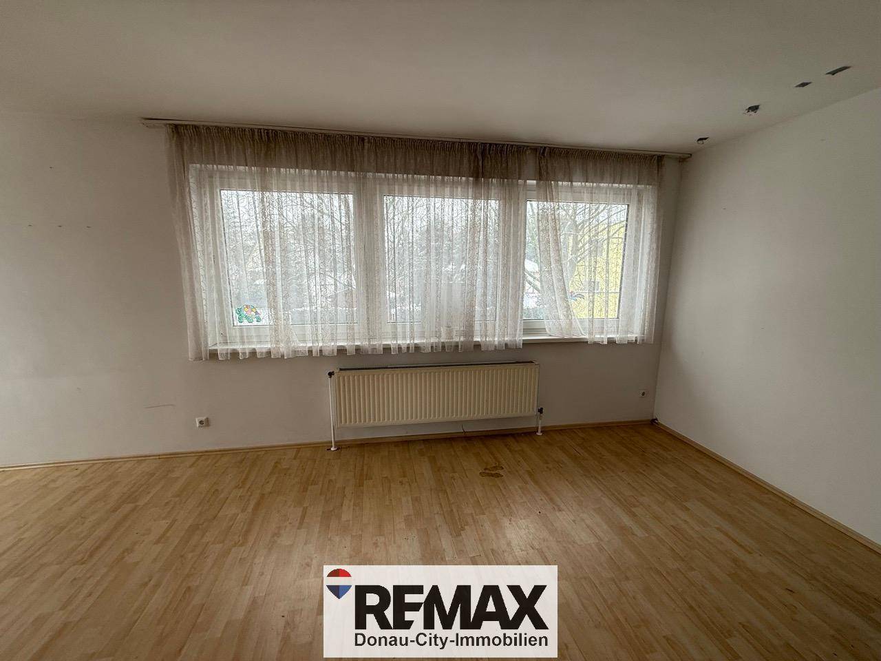 Leeres Wohnzimmer mit Laminatboden und großen Fenstern, die für eine helle Atmosphäre sorgen.