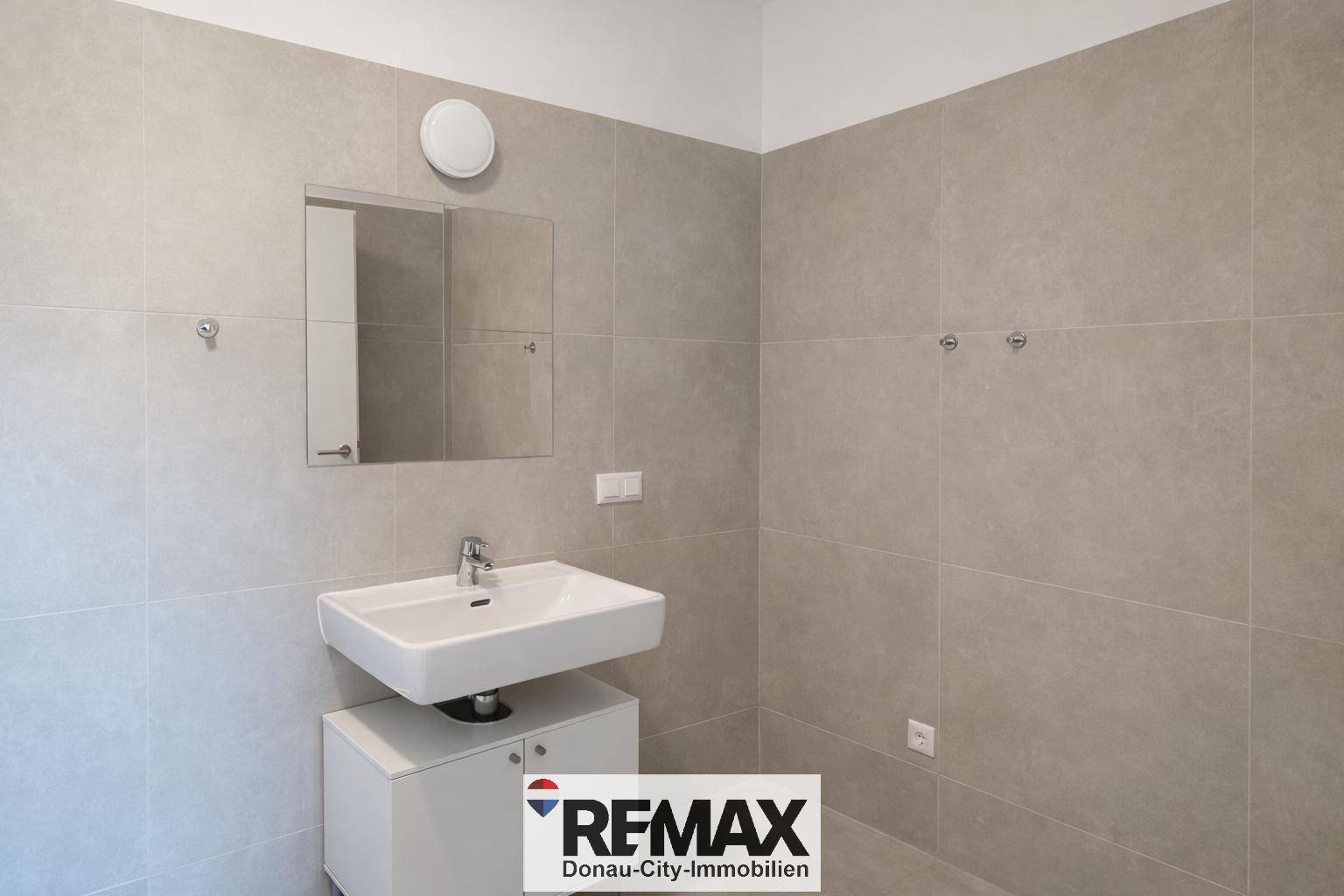 Modernes Badezimmer mit großformatigen grauen Fliesen und Einzelwaschbecken.