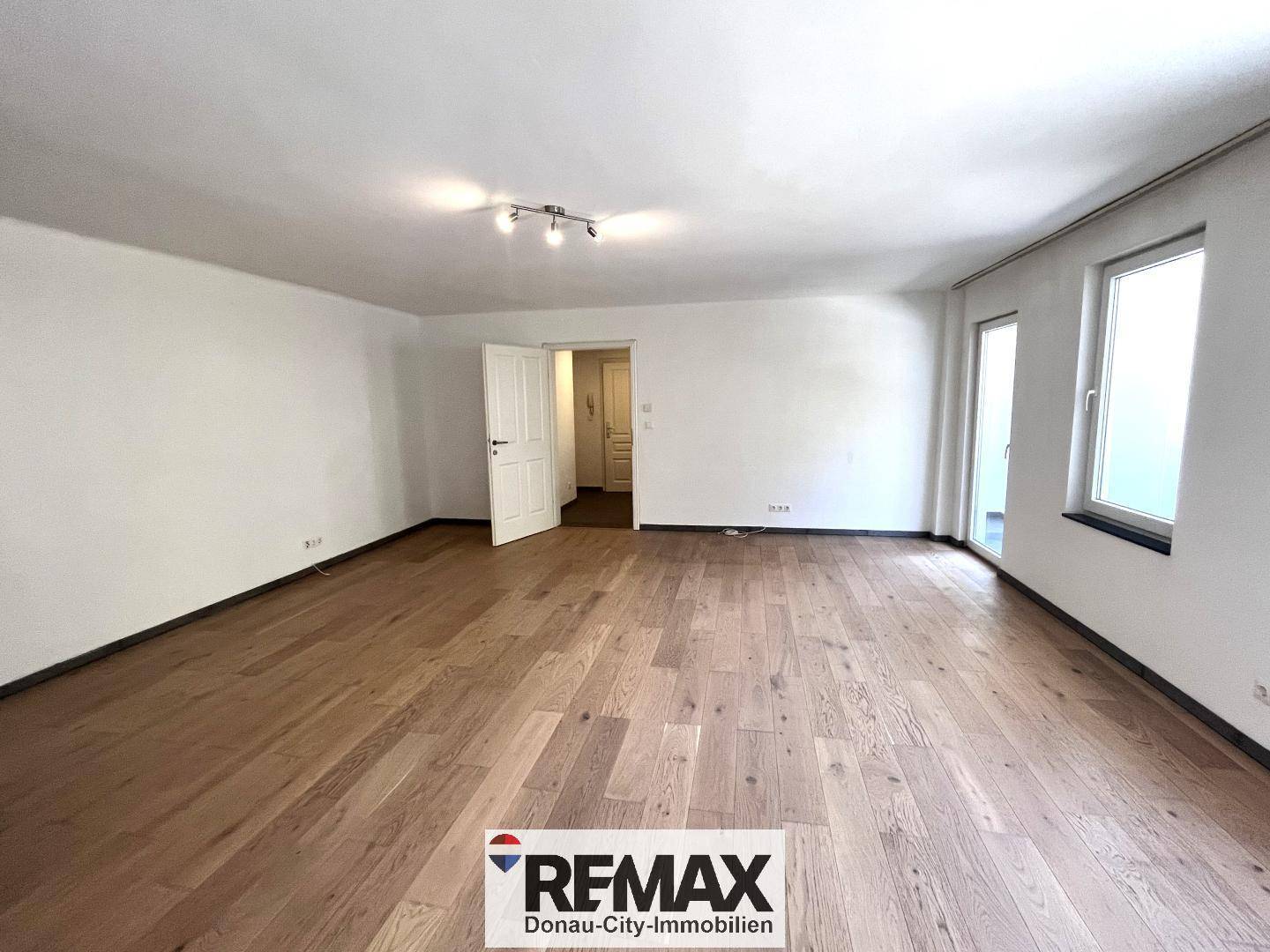 Großes, helles Wohnzimmer mit Holzboden und Zugang zu einem weiteren Bereich.