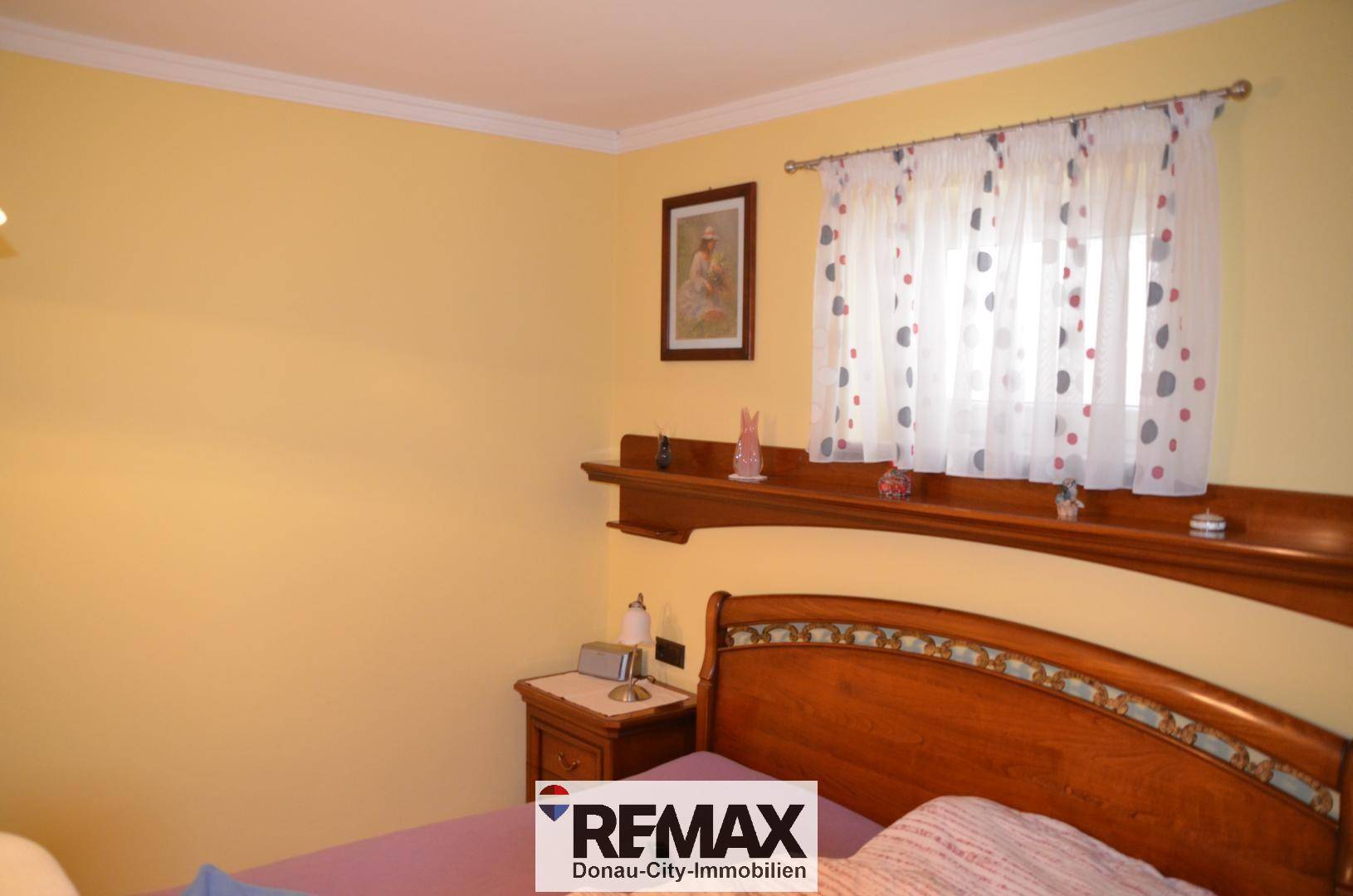 Schlafzimmer mit gelben Wänden, einem Holzbett und einem Fenster mit Vorhängen, das für Helligkeit sorgt.