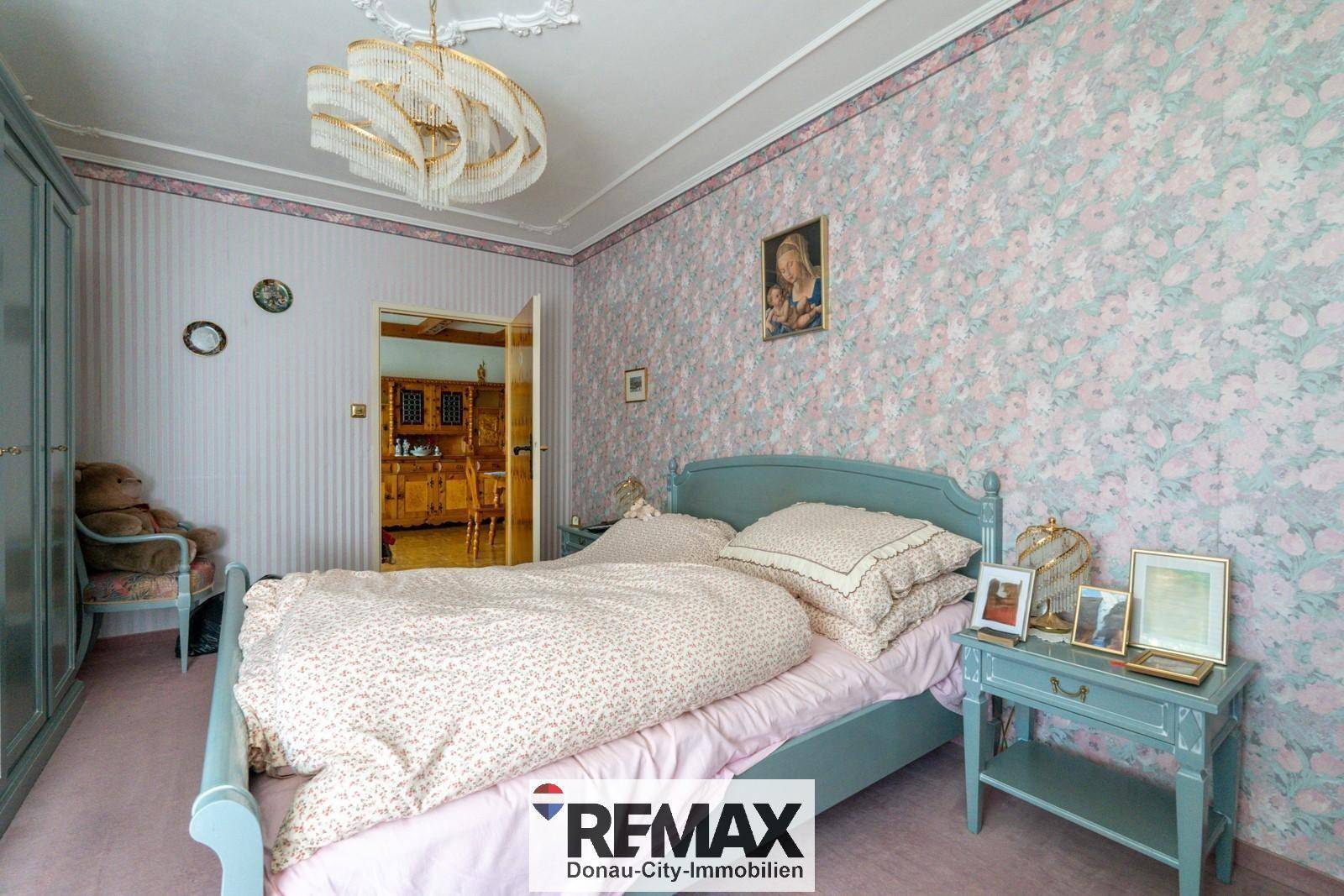 Gemütliches Schlafzimmer mit floraler Tapete, hellblauem Bett und Nachttisch.