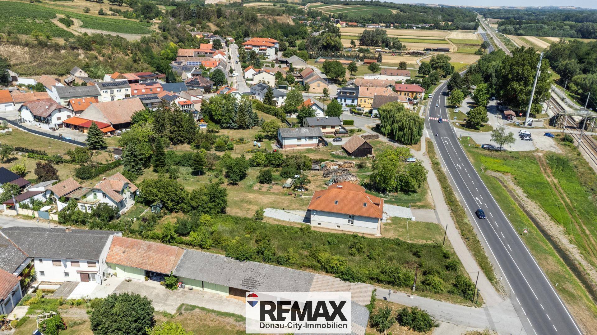 Weitläufige Luftaufnahme eines Dorfes mit Häusern, Straßen und viel Grün in ländlicher Umgebung.