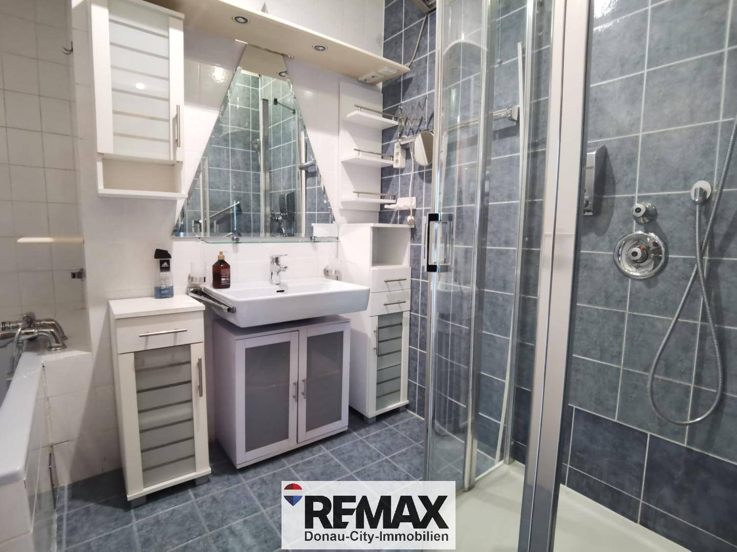 Badezimmer mit Duschkabine, modernem Waschbecken und blaugrauen Fliesen.