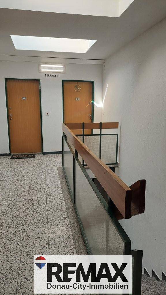 Heller Treppenhausflur mit Terrazzoboden, Holzgeländer und Zugang zu den Wohnungen.