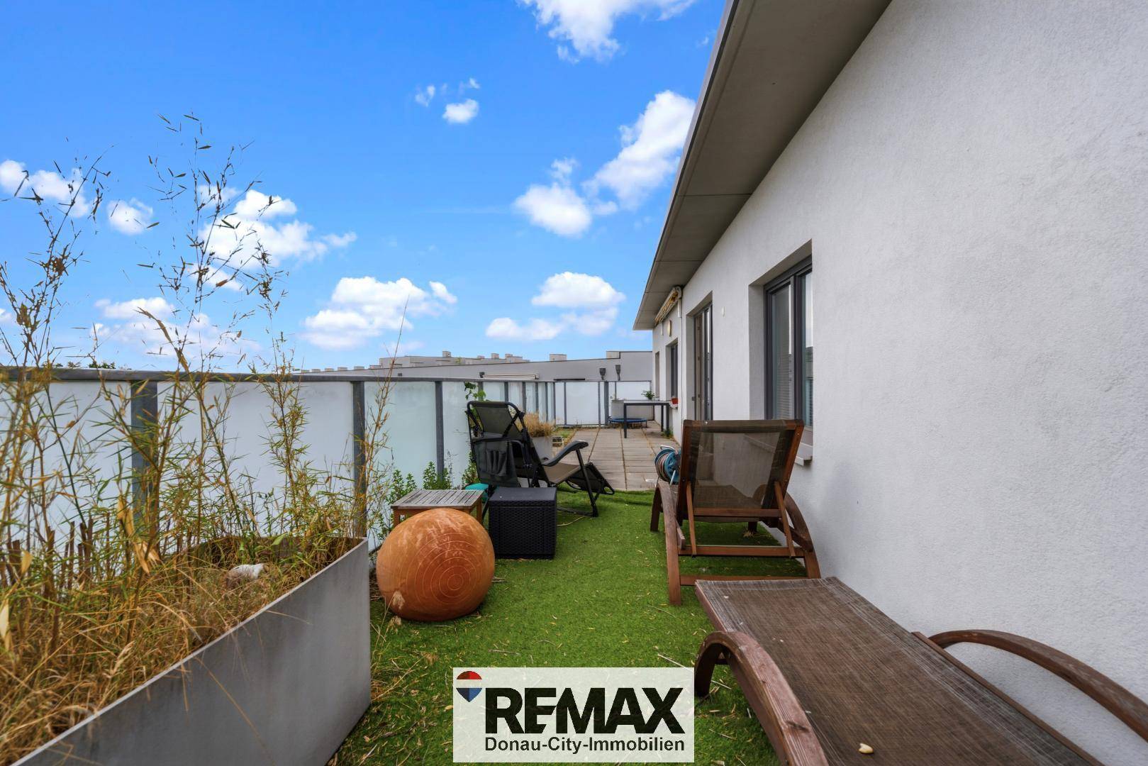 Dachterrasse mit Kunstrasen, Liegestühlen und Pflanzen in Kübeln.