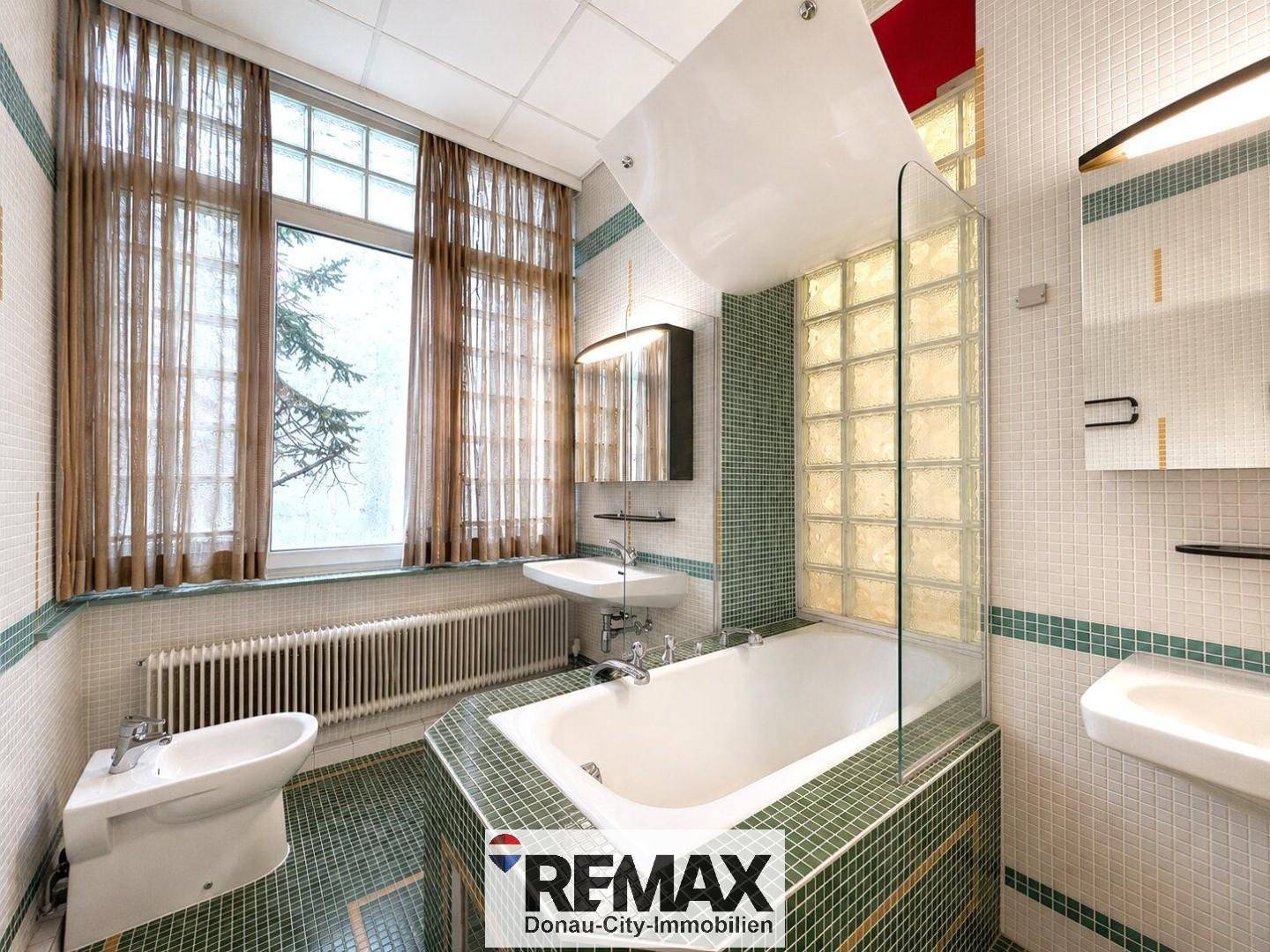 Badezimmer mit Badewanne, Bidet und Waschbecken, ausgestattet mit grünen und weißen Fliesen.