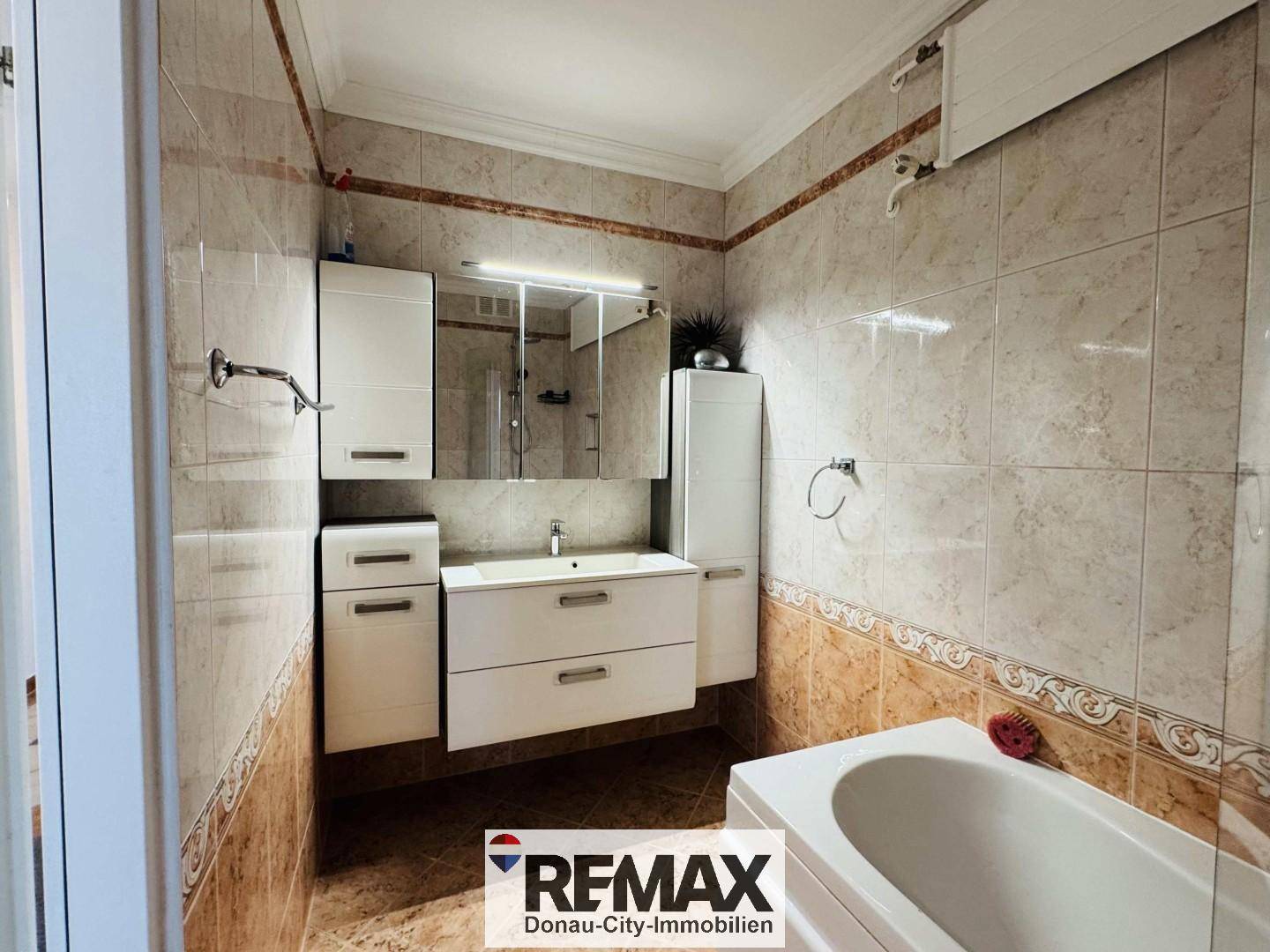 Gefliestes Badezimmer mit Badewanne, Waschtisch und Spiegelschrank.