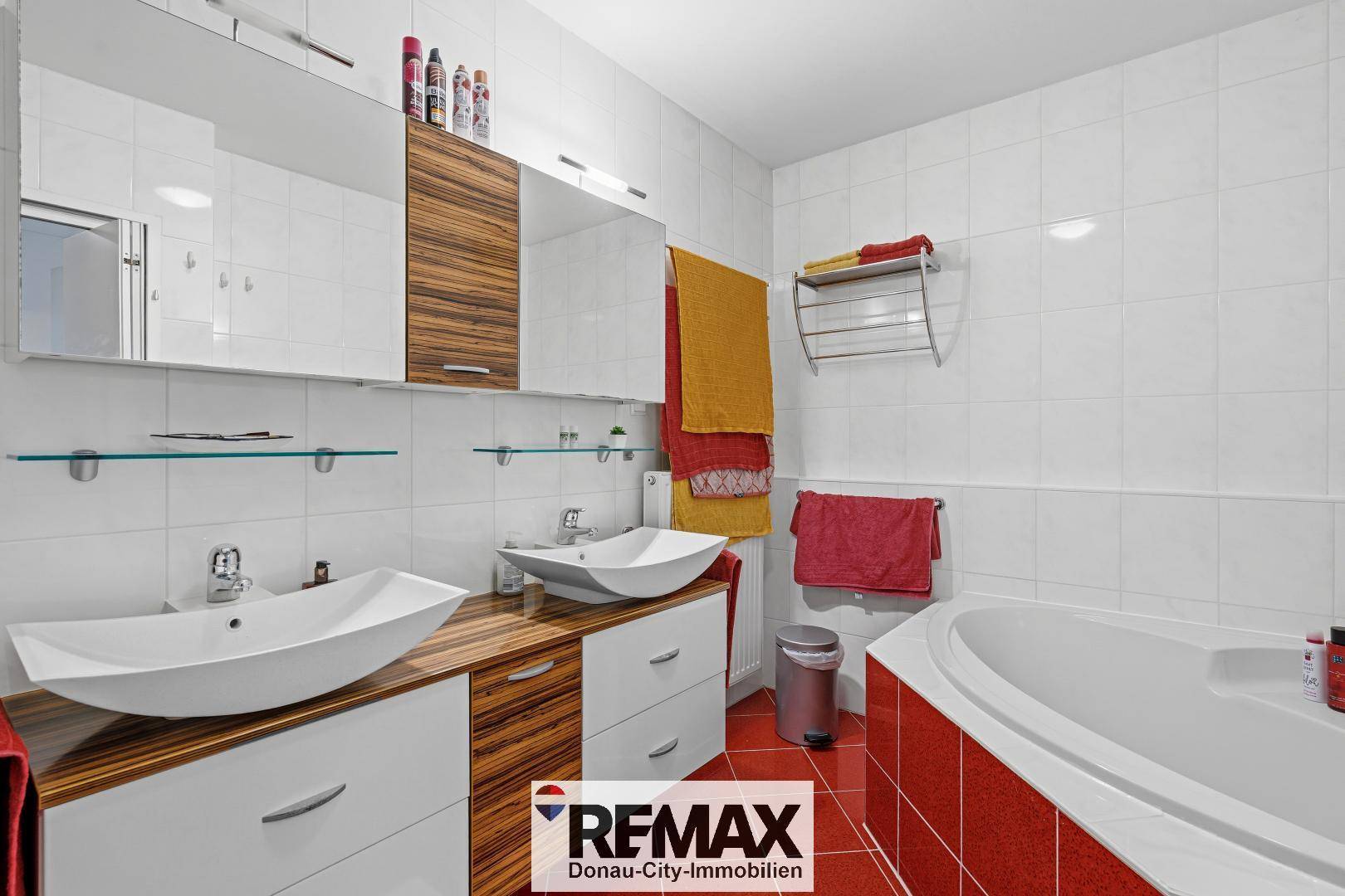 Modernes Badezimmer mit Doppelwaschbecken, Badewanne und roten Bodenfliesen.