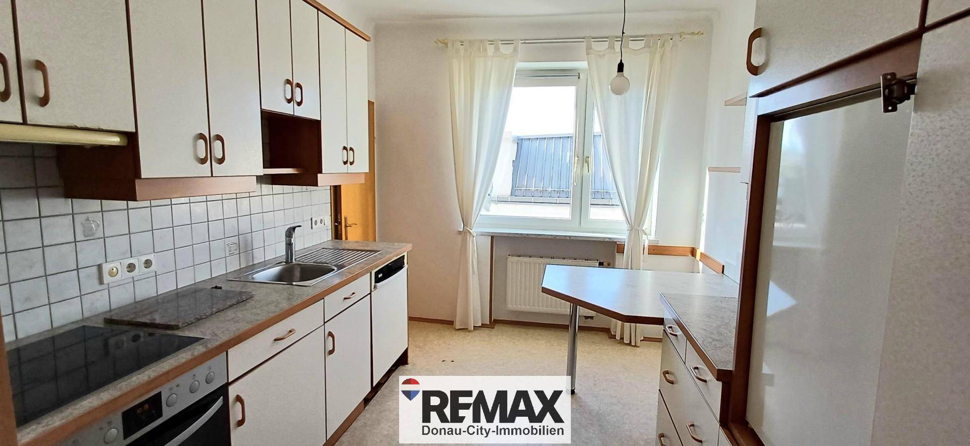 Funktionale Küche mit weißen Schränken, Fliesenrückwand und einem Fenster mit Vorhängen.