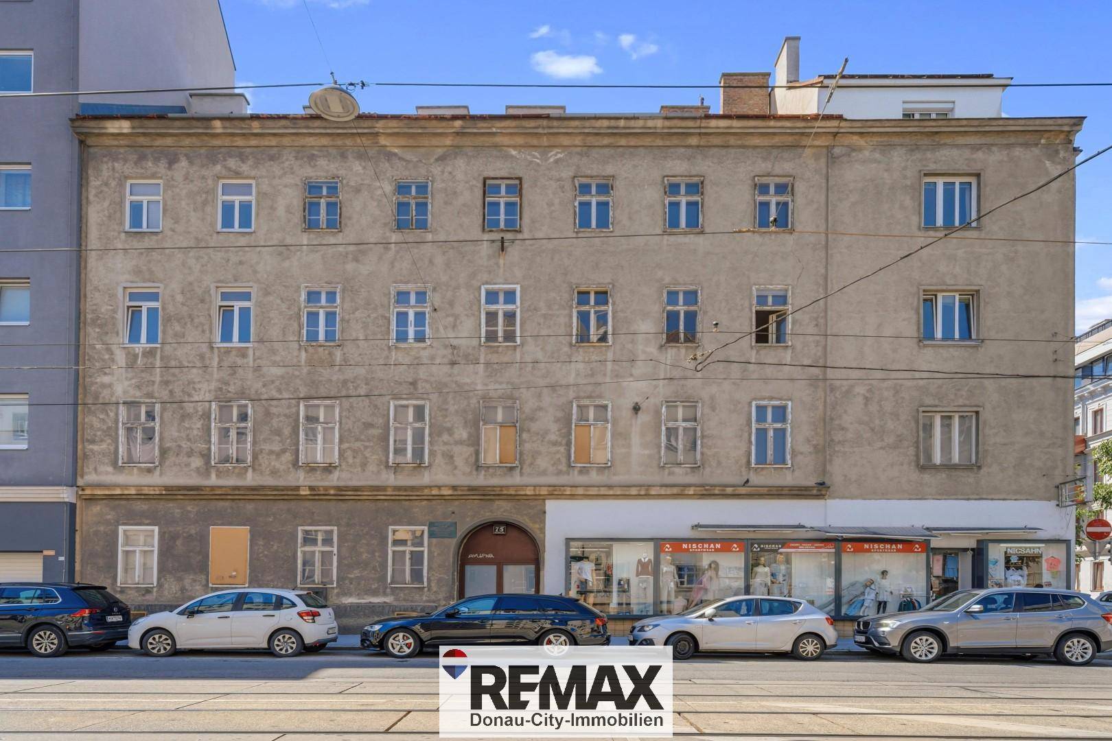 Historische Fassade eines Altbaus an einer belebten Straße mit parkenden Autos.