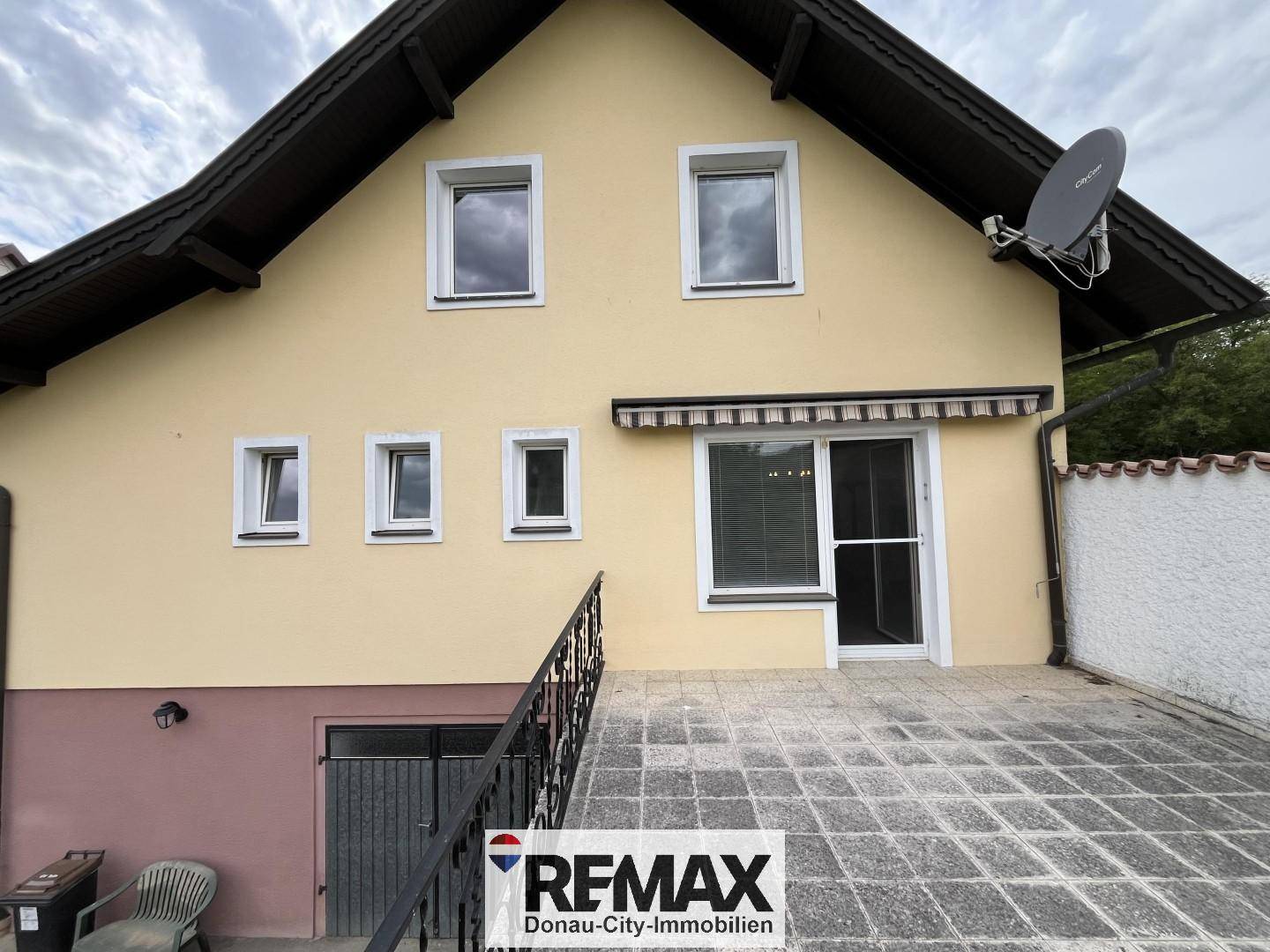 Rückseite des Hauses mit gefliester Terrasse, Treppe und Satellitenschüssel.