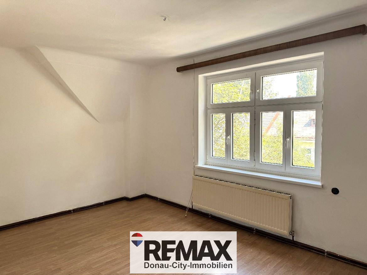 Helles, leeres Zimmer mit weiß gestrichenen Wänden, großem Fenster und Laminatboden.